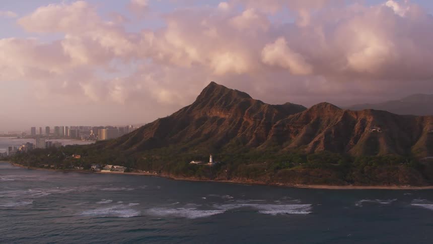 Lighthouse sits in forest between beach and mountain with fog covered cove and city in background under cloudy sky