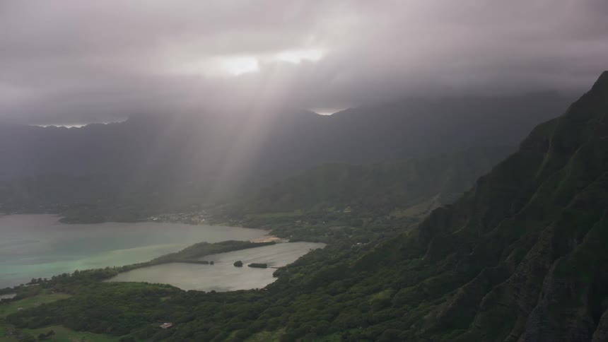 Sun beams break through heavy cloud cover to shine on oceanside mountains and slopes