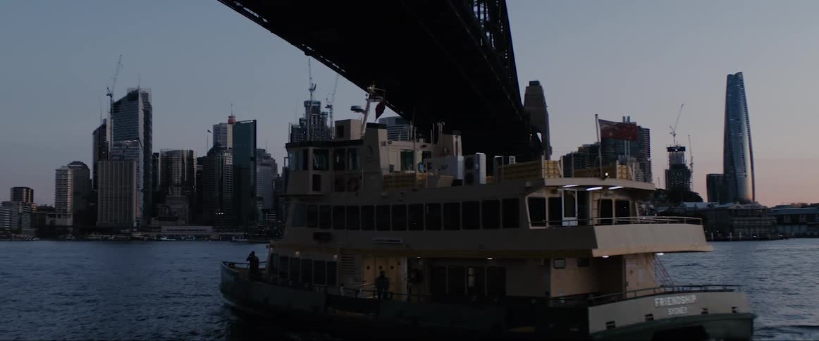 Small ferry driving under a bridge over a river near the city skyline at morning