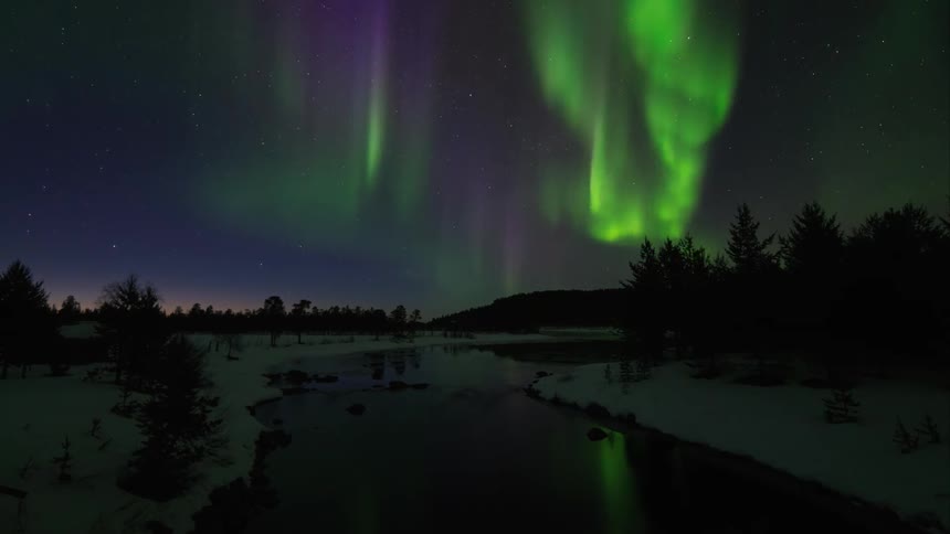 Purple and green aurora borealis in a winter sky over a still river