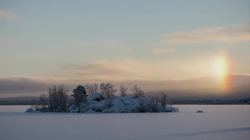 Timelapse of rocky island rainbow on a frozen lake in Finland