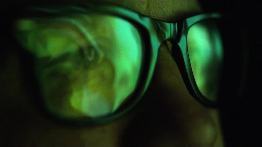 A person in a room with glasses with light reflecting off of it and a wall in the background