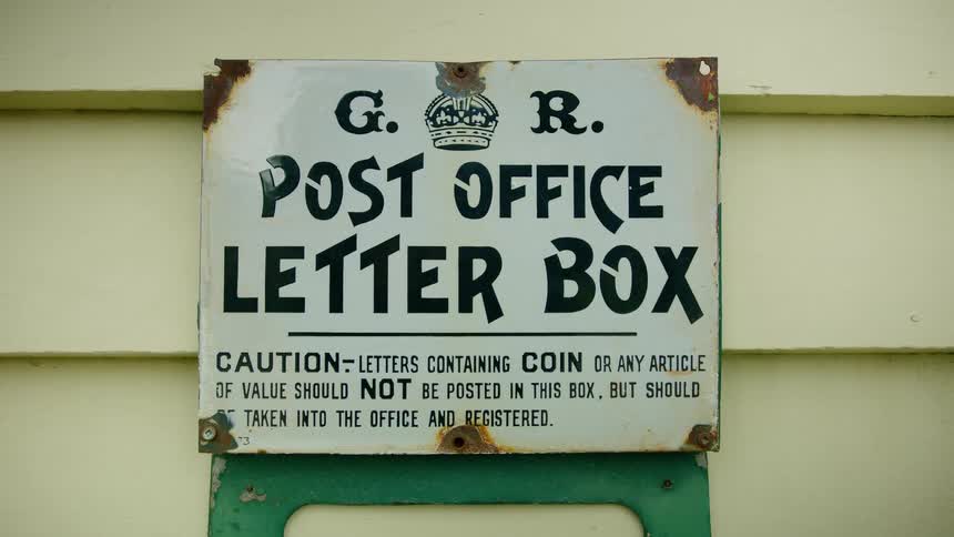 A close view of an old metal post office sign posted outside in the daytime