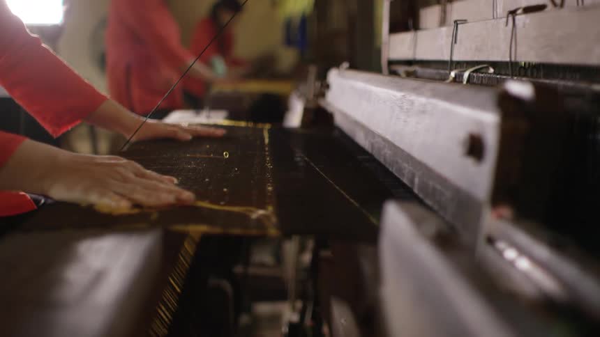 People are weaving material in a large room