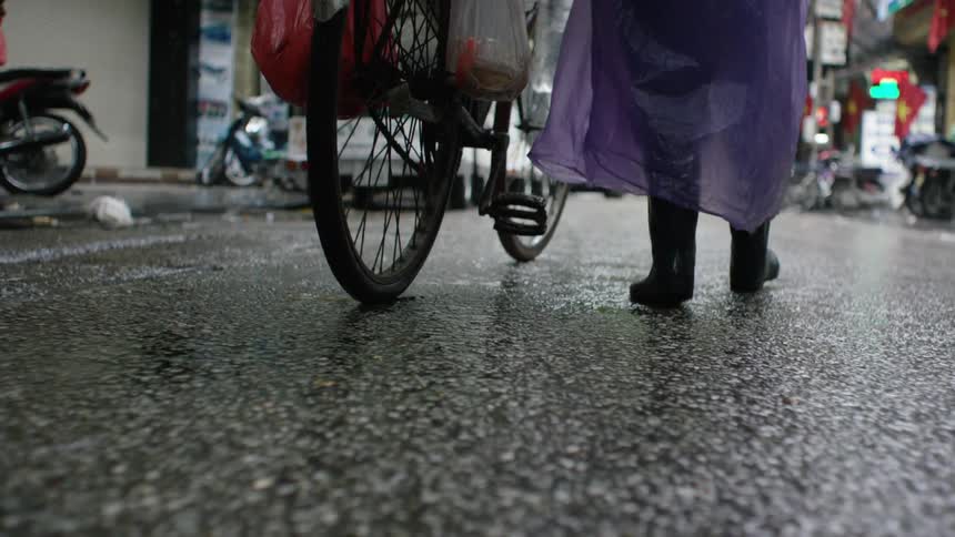 Man wearing a purple raincoat pushes a bicycle on a wet city street