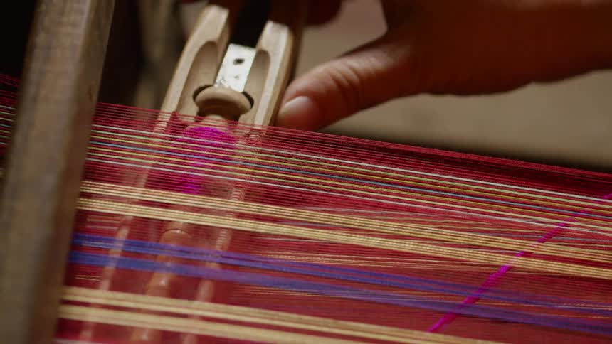 Woman pushes a yarn carrier inside a loom with colorful threads