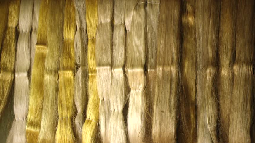 A light illuminates an inventory of blonde human hair hanging in a closet