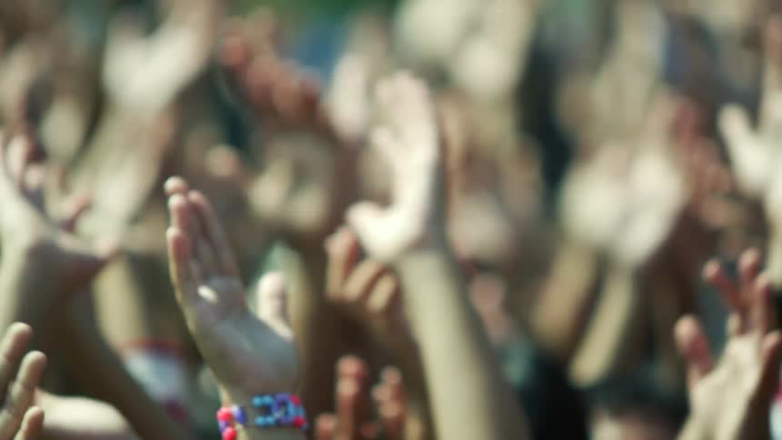 People in a crowd clapping their hands with trees and buildings in the background