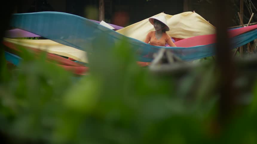 Asian woman stand outside and hold long pieces of cloth and lift it up in the air and back down again