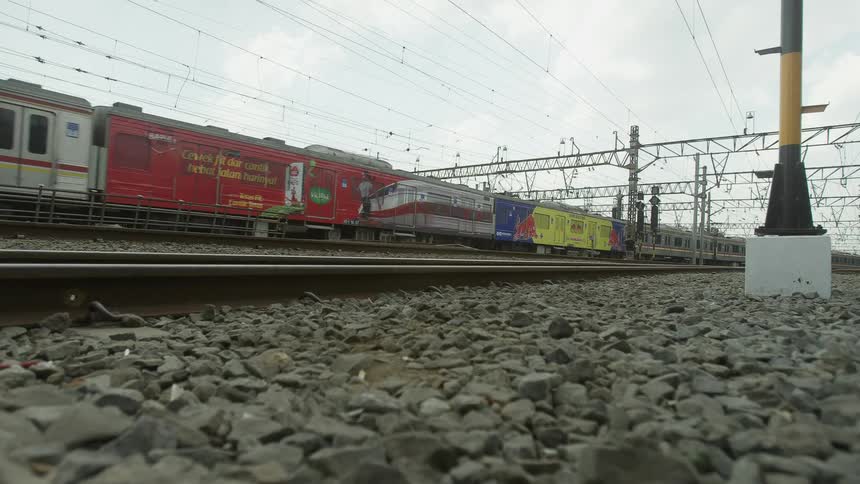 A train running on train tracks with gravel in the foreground and the sky and clouds in the background