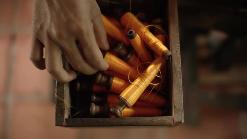 A person grabbing a spool of thread out of a box
