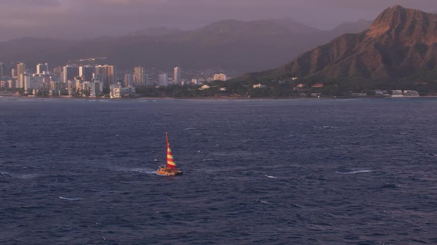 A sailboat sails through the water with a city skyline and mountains in the background