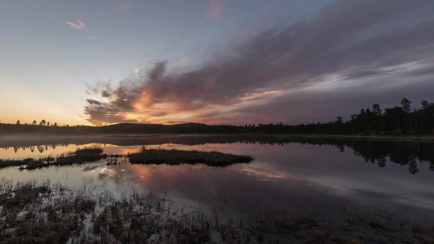 Slow moving clouds at sunset over a reflective lake, time lapse
