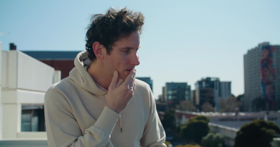 A man is typing while sitting of a rooftop ledge in an urban area during the daytime