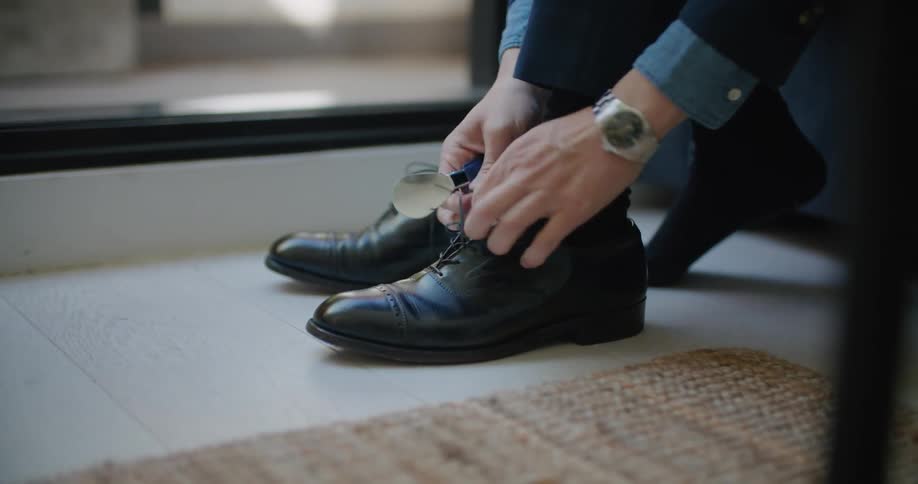 A man uses a shoehorn to put on a shoe before tying it