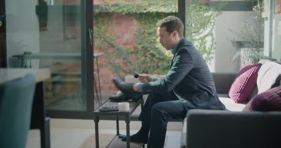 A man sits on a couch and polishes his shoes