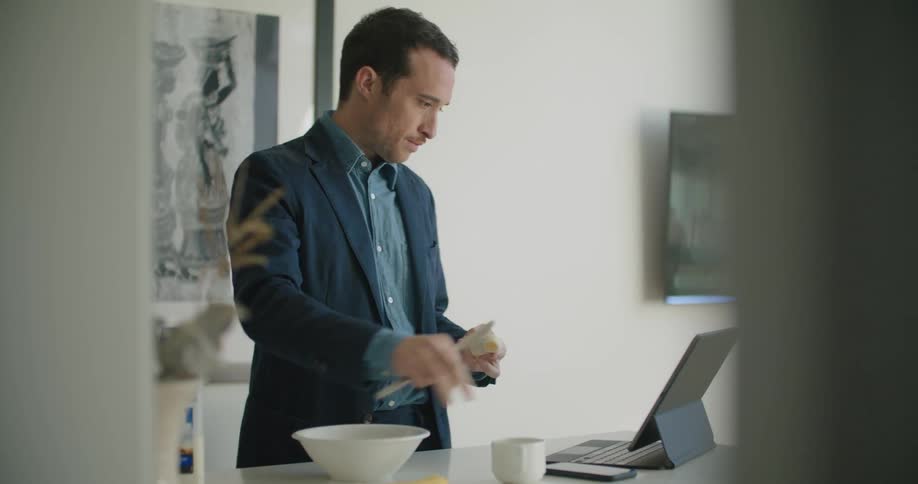 A man stands by a tablet computer and peels a banana into a bowl