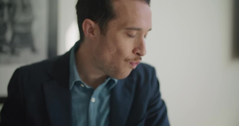 A man sits at a table at home and eats as he looks at his laptop