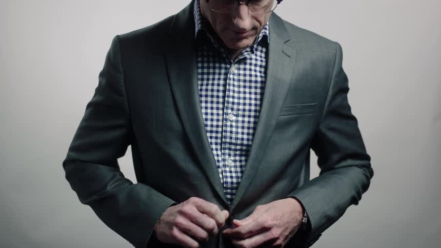 A man looks down buttoning his blazer