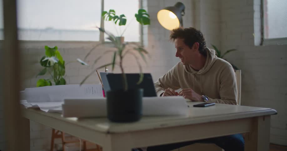 Young man sitting at a desk greeting someone on a video call on a laptop