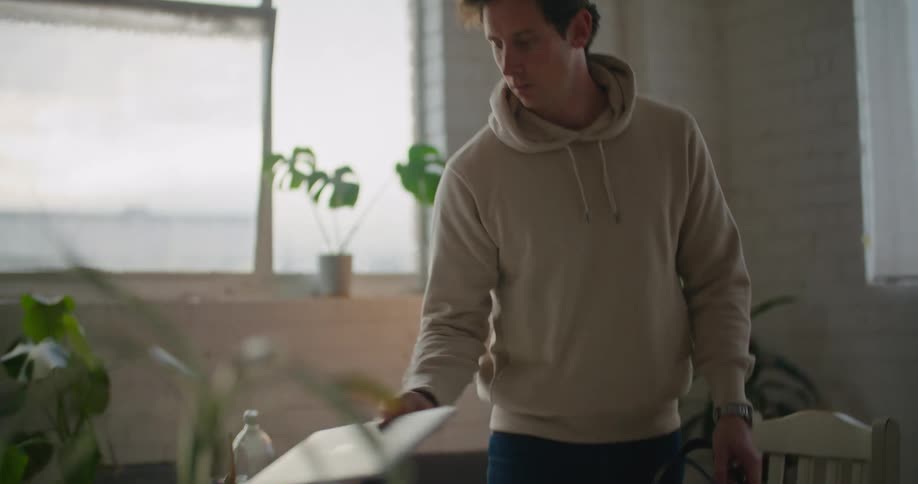 A man removes a laptop from his backpack and places it on a table desk