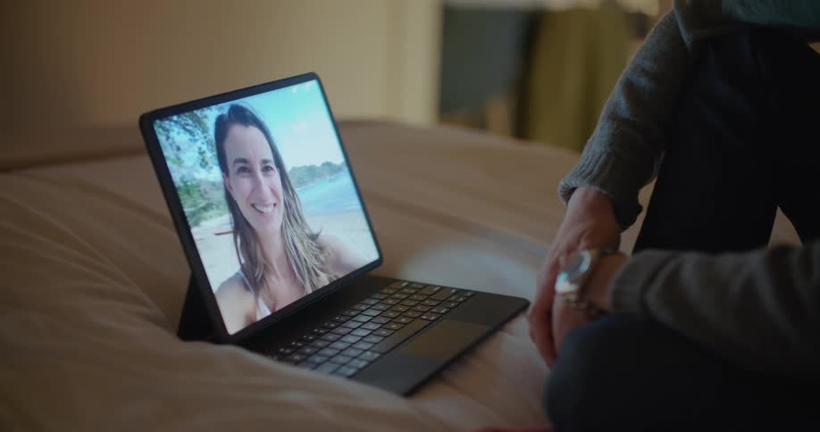 A person sits on a bed having a video call with a female