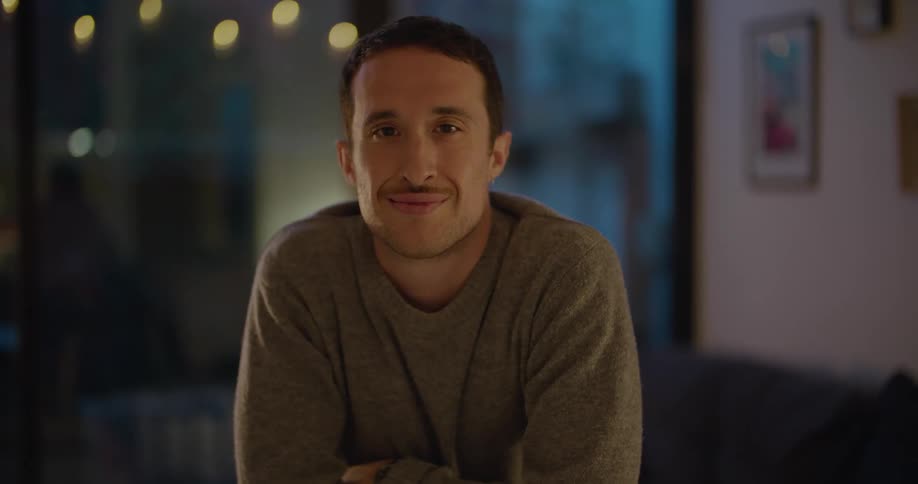 A man in a room staring with a wall a couch and a picture frame in the background