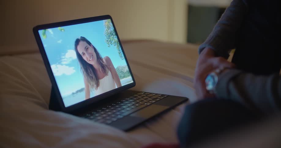 Young woman on a beach talking to her boyfriend sitting in a bed at home on a video call