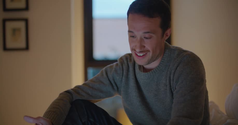 A man sits on a bed having a video call on a laptop