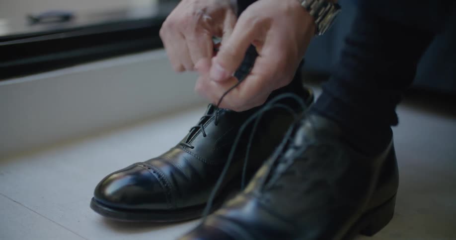 A man uses a shoe horn to put on his shoe then ties his laces