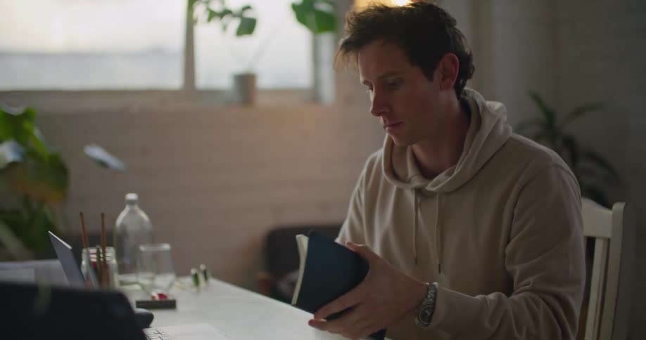 Young man working on a laptop grabs a notebook to take notes