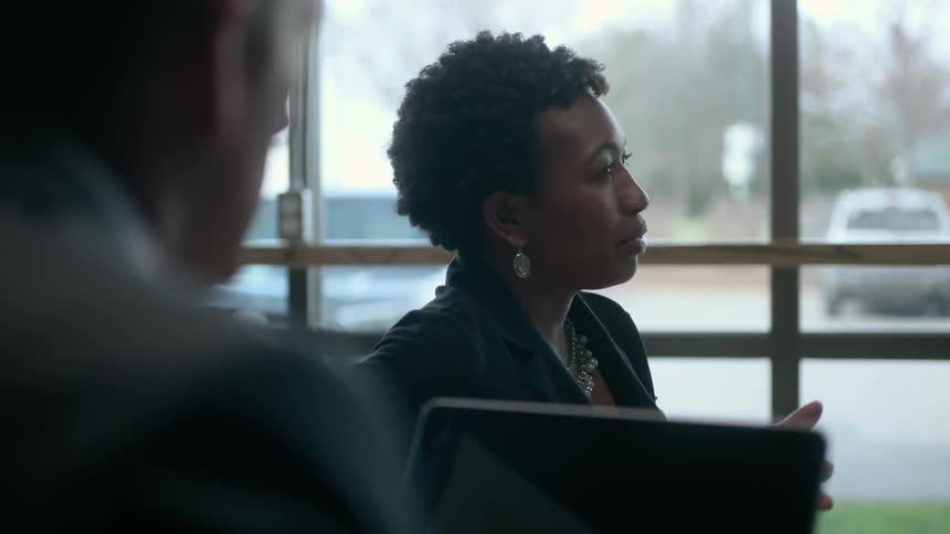 A woman talks as a man sits nearby