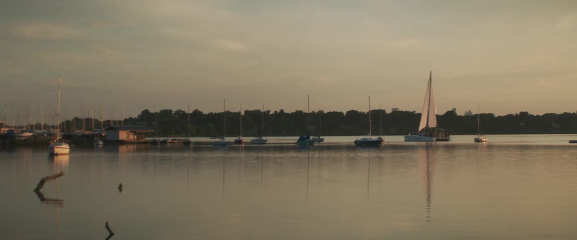 Boats driving on the calm surface of a lake near a pier at sunset