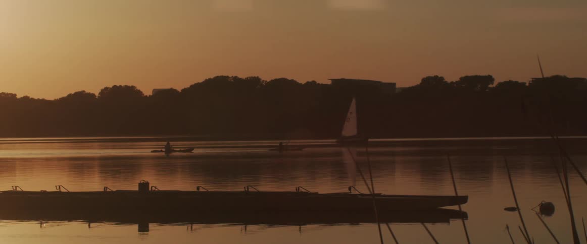 People paddling kayaks on a lake near a boat at sunset