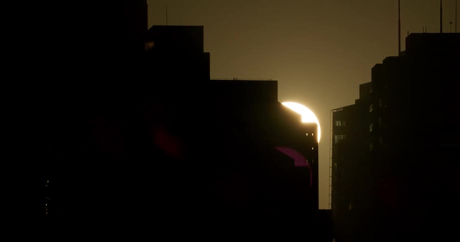 A city with silhouettes of buildings with the sun the sky and clouds in the background