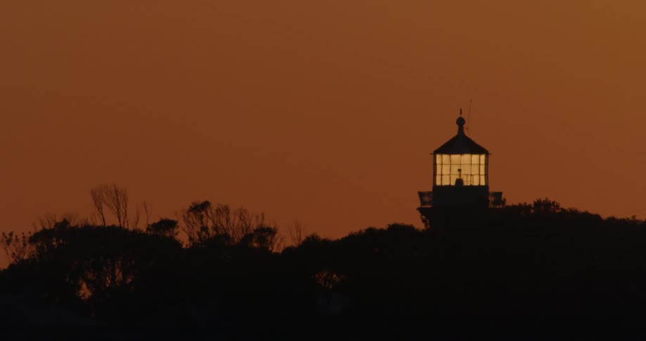 The top of a lighthouse is silhouetted against a hazy red sky