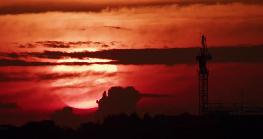 Huge sun in crimson sky casts construction site into silhouette