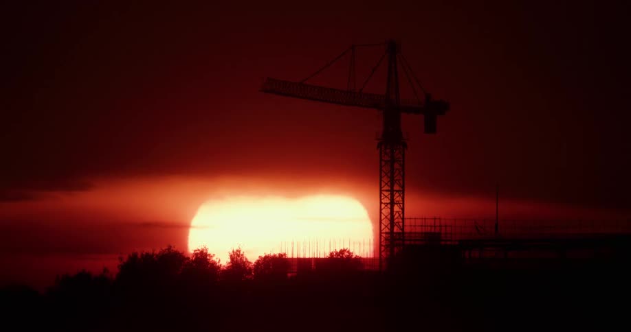 The sun is very low on the horizon behind a construction crane