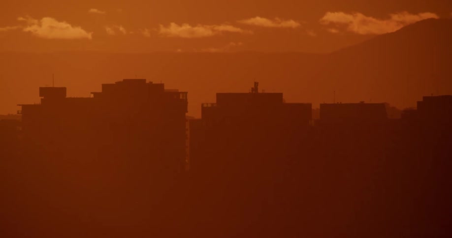 The silhouette of city buildings against an orange hazy sky