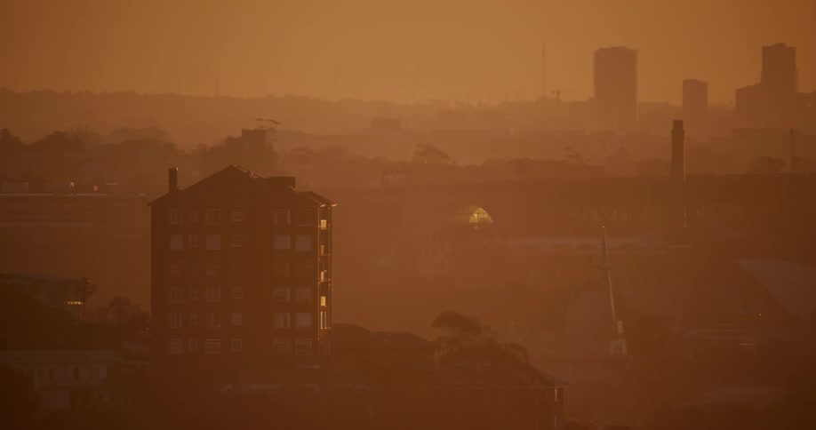 A yellow haze glows in a landscape buildings and hills as cars travel across a bridge