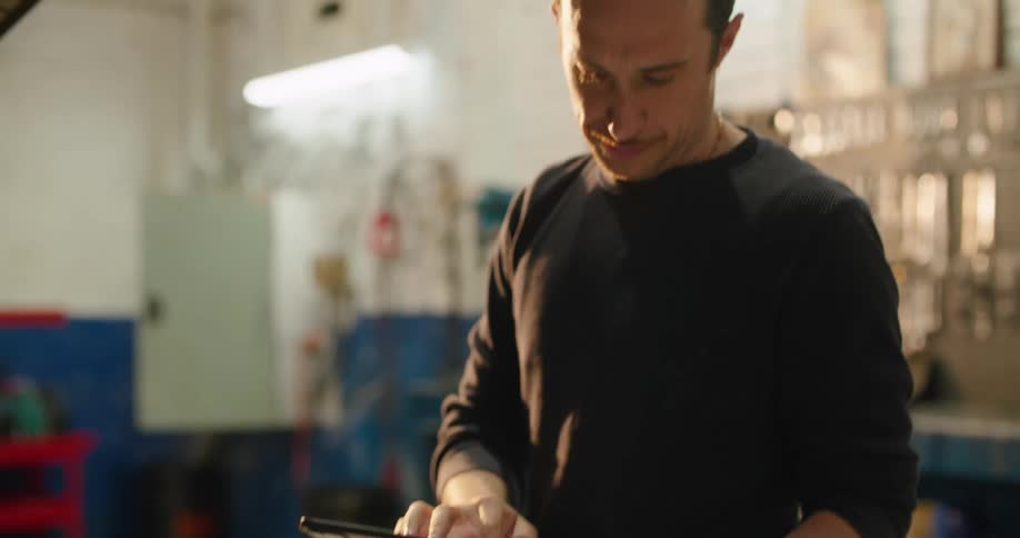 A mechanic leads over a car looking at a tablet