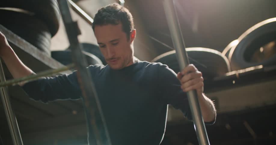 A man in a garage walking up a ladder with tires and a wall in the background