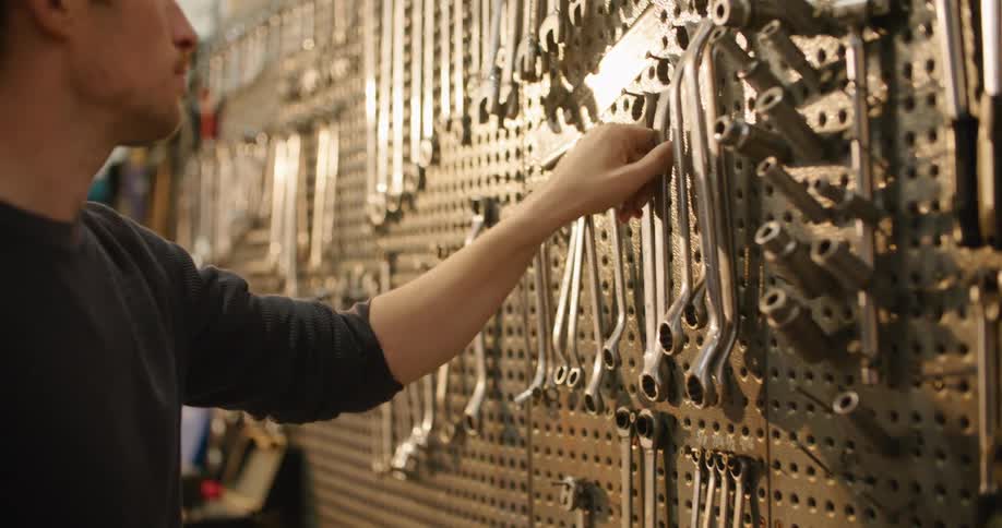 A man chooses a wrench from a wall in his workshop