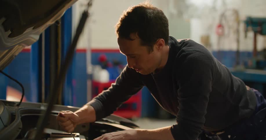 A man tightens a bolt on a car engine with his fingers for a moment before switching to using his wrench