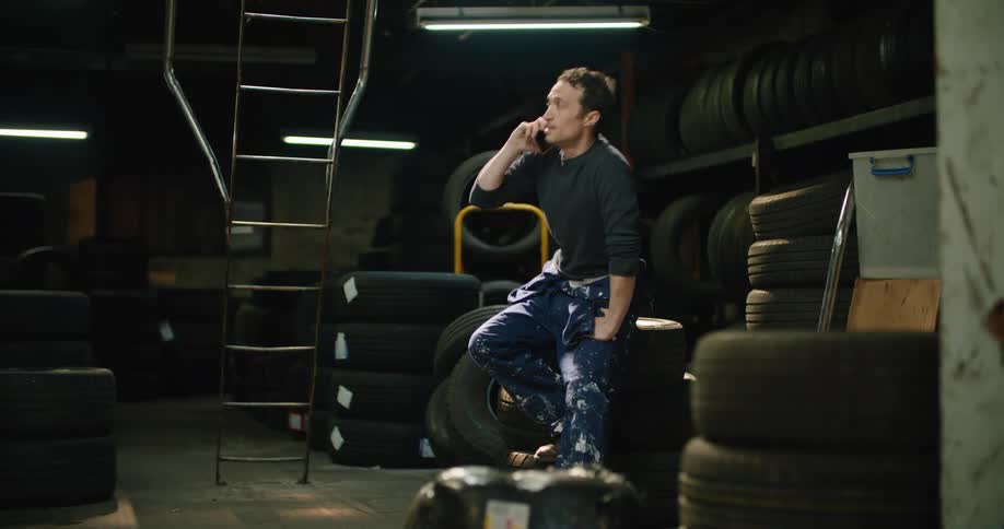 Man sitting on a pile of tires inside a warehouse talking on his phone