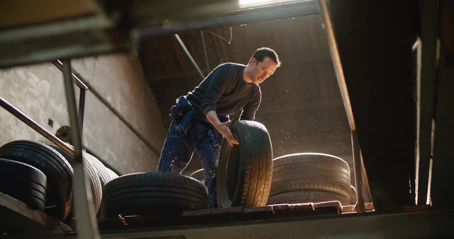 A man in a room picking up a tire with a wall and ceiling in the background