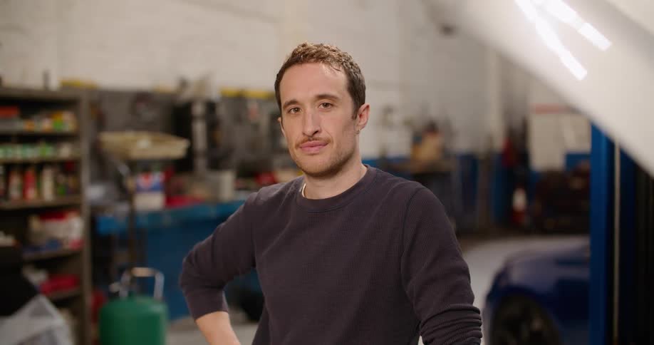 A man in a garage with a vehicle shelves and a wall in the background