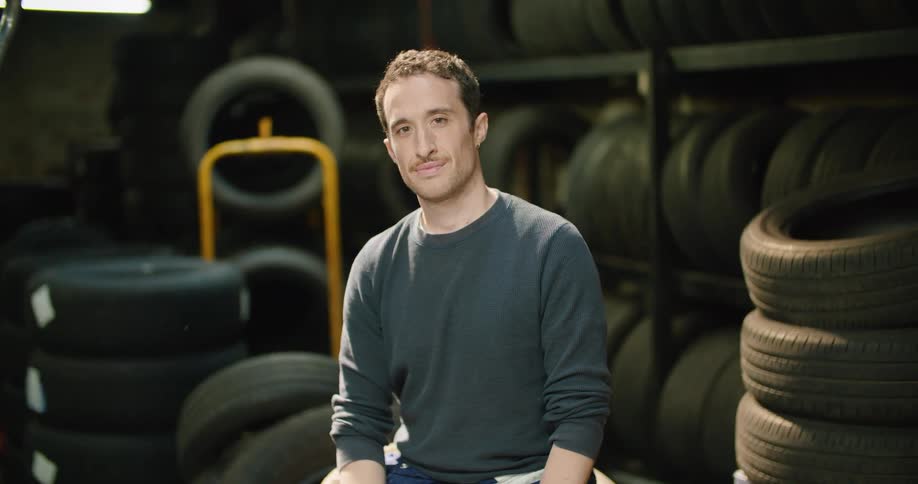 Young man sitting over a pile of tires looks at the camera smiling