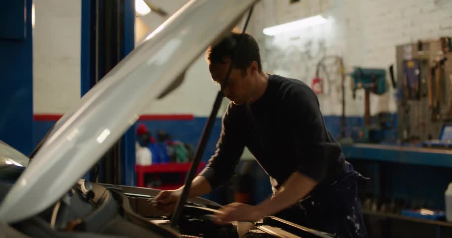 A man in a garage working with a tool under the hood of a vehicle with a wall in the background