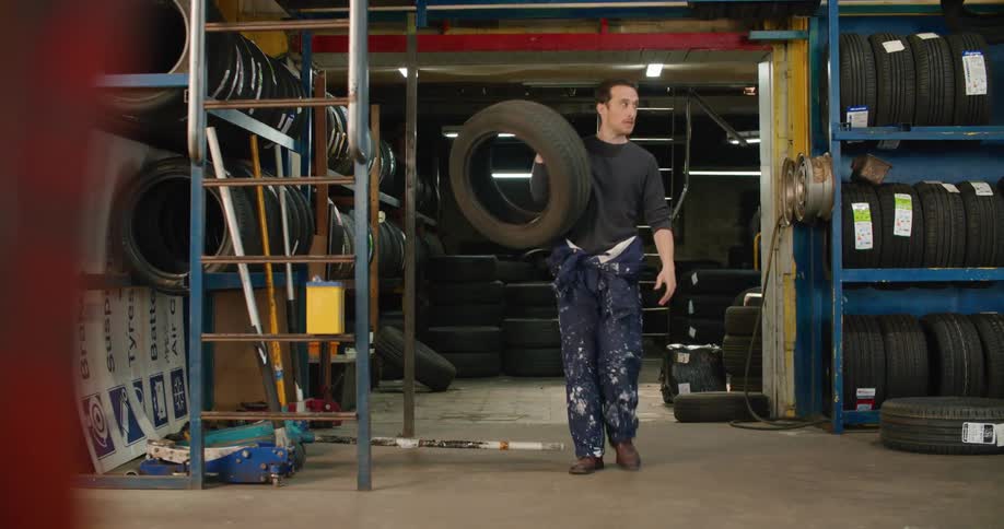 A man moving a car tire out of a warehouse